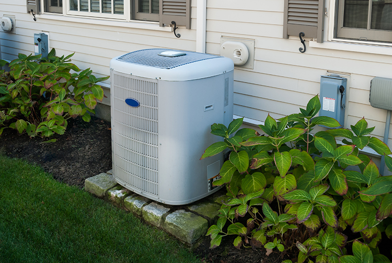 Air conditioner unit outside a house next to some greenery.