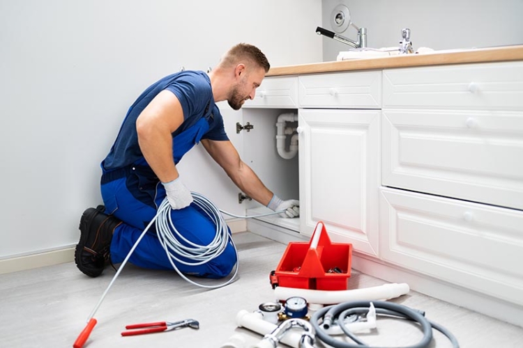 Male plumber cleaning a pipe under a sink with tools.