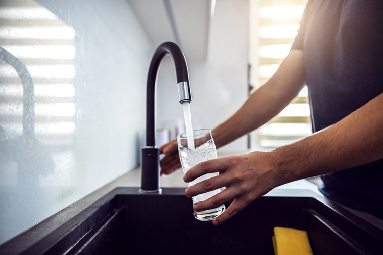 Close up of man filling a glass with clean water from the kitchen faucet.