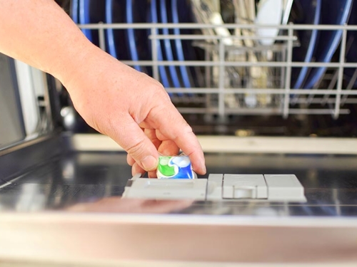 Man placing a detergent pod in dishwasher.