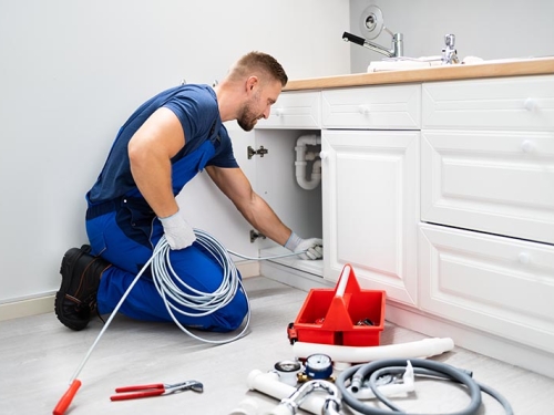 Male plumber cleaning a pipe under a sink with tools.