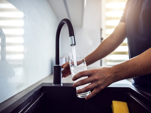 Close up of man filling a glass with clean water from the kitchen faucet.