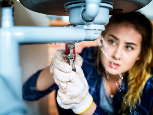 Woman trying to fix a leaking pipe under a sink.