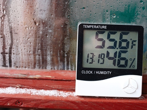 Thermometer showing 55.6°F and 46% humidity near a wet window.