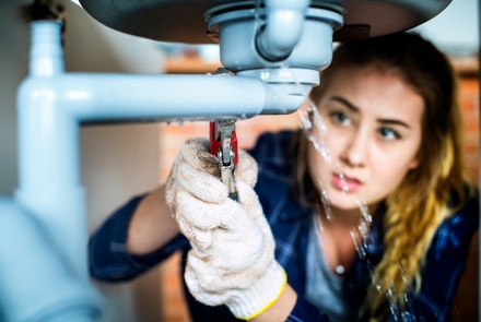 Woman trying to fix a leaking pipe under a sink.