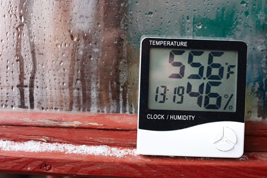 Thermometer showing 55.6°F and 46% humidity near a wet window.